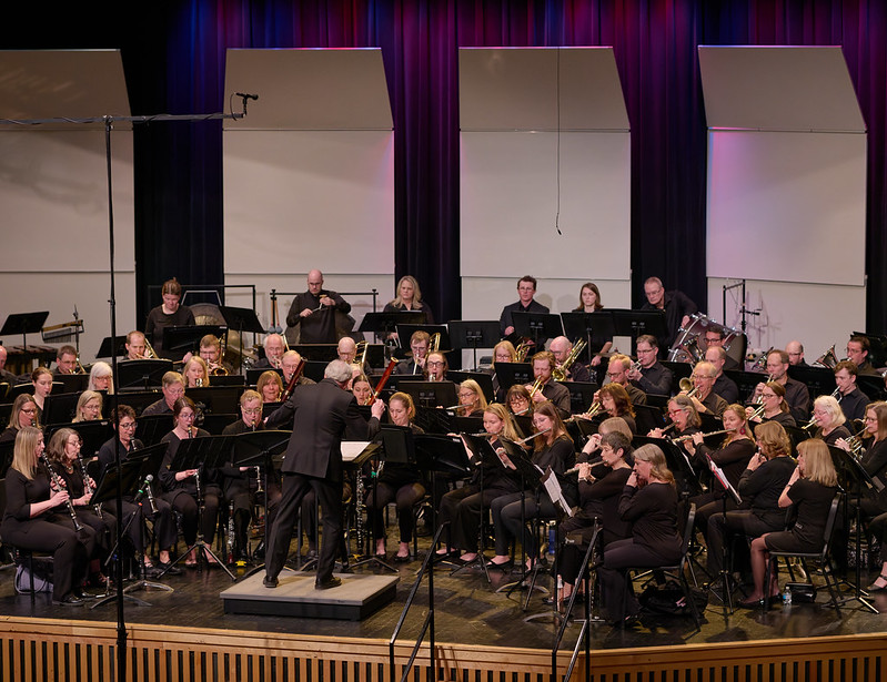 A color photograph of the ensemble performing on a stage. The view is from the upper right side of the hall looking downwards.
