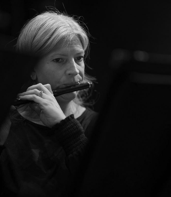 A black and white image of a woman playing piccolo in black concert attire. 